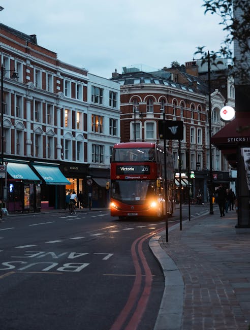 A red double-decker bus displaying route number 26 and destination Victoria is approaching a bus stop on a city street in Belgravia, near Victoria Station. Surrounding buildings feature traditional wh